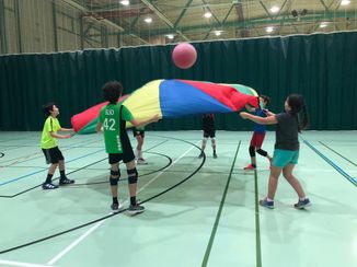 Des enfants jouant avec un grand drap circulaire et une grosse balle